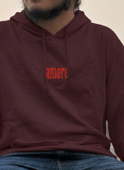Person wearing a maroon hoodie with 'amore' text and a matching bandana, sitting outdoors.