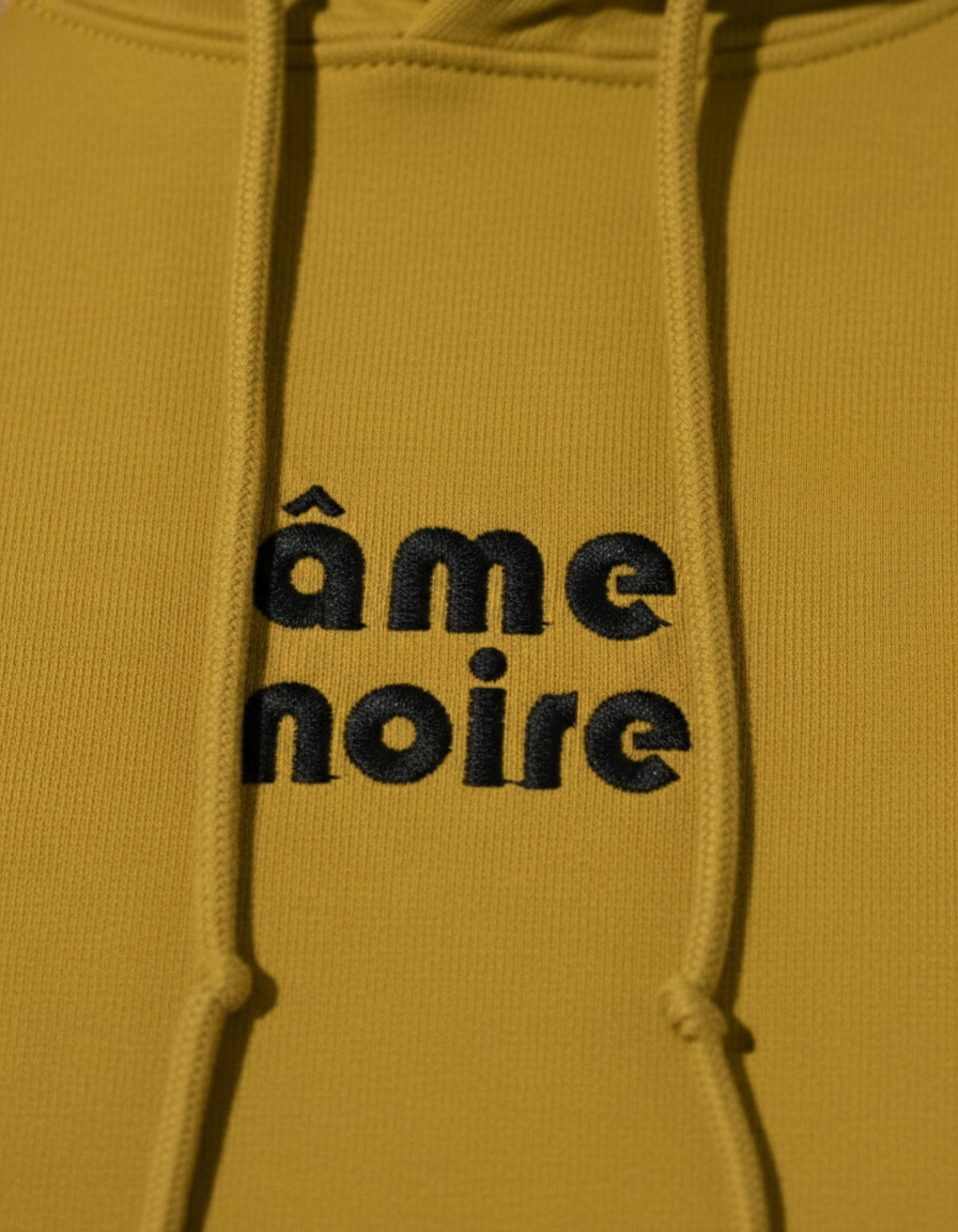 Mustard yellow hoodie with 'âme noire' text in black on a matching background