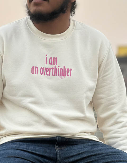 Person wearing a white sweatshirt with 'i am an overthinker' text and a red turban sitting outdoors.