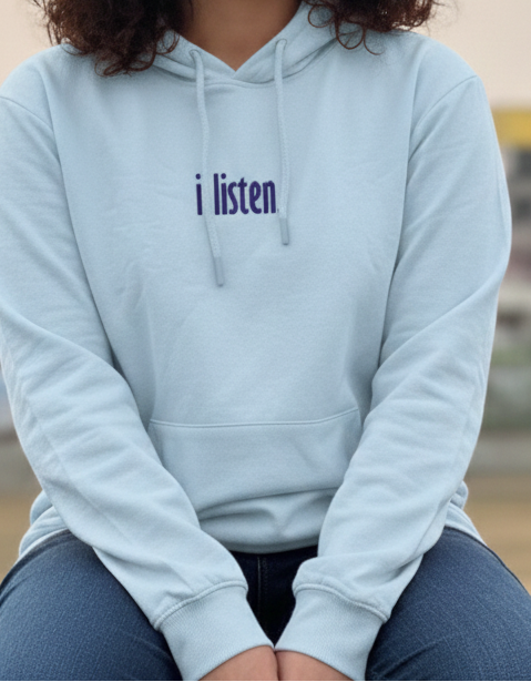 Woman wearing a light blue hoodie with 'i listen' text, sitting outdoors.